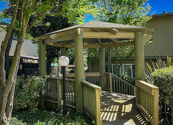 A wooden gazebo with a white ball on top is surrounded by greenery.