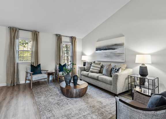 A living room with a grey couch, a coffee table, and a large painting on the wall at West Oak Apartments, Wake Forest
