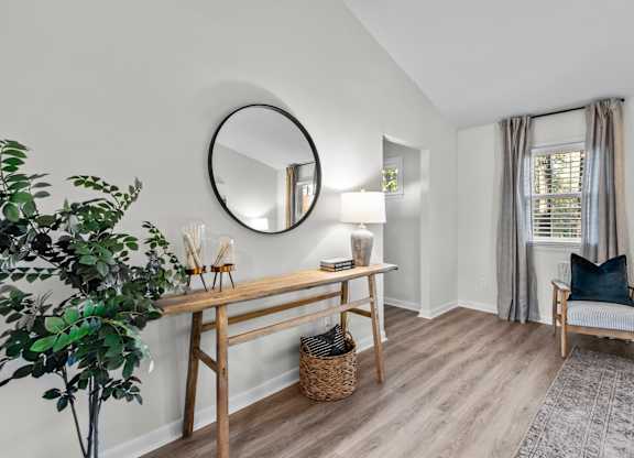 A room with a round mirror, a wooden table, a chair, and a potted plant at West Oak Apartments, Wake Forest, 27587