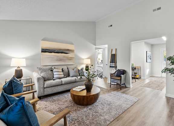 A living room with a grey couch, a wooden coffee table, and a large painting on the wall at West Oak Apartments, Wake Forest, NC 27587