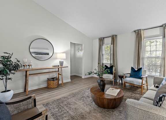 A living room with a grey couch, a wooden coffee table, and a mirror on the wall at West Oak Apartments, North Carolina