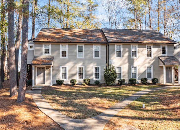 A large house with a grey roof and white walls is surrounded by trees at West Oak Apartments, Wake Forest, 27587