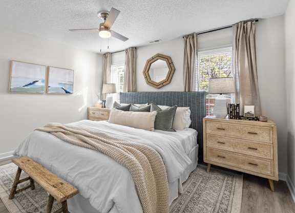 A bedroom with a bed, a bench, a dresser, and a ceiling fan at West Oak Apartments, Wake Forest, North Carolina