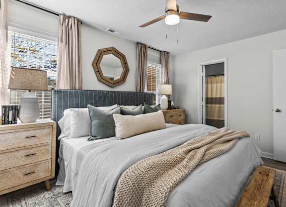 A bedroom with a large bed, a ceiling fan, and a mirror on the wall at West Oak Apartments, Wake Forest, NC 27587