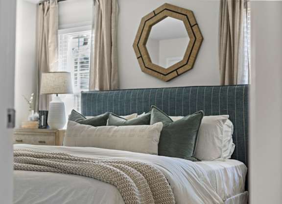 A bedroom with a bed, pillows, a mirror, and a lamp at West Oak Apartments, North Carolina 27587