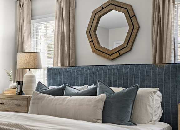 A bedroom with a bed, pillows, a mirror, and lamps at West Oak Apartments, Wake Forest, 27587