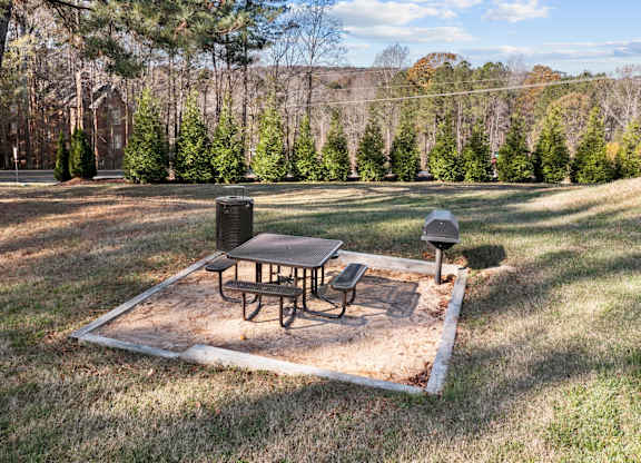 A picnic table and two chairs are set up on a picnic table in a grassy area at West Oak Apartments, Wake Forest
