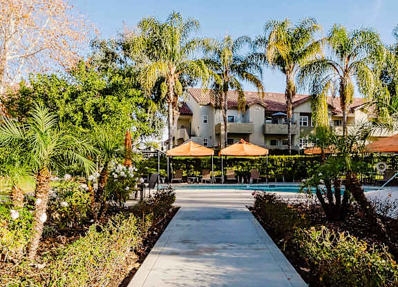 A pathway leads to a building surrounded by palm trees. at Legends at Rancho Belago, Moreno Valley, CA, 92553