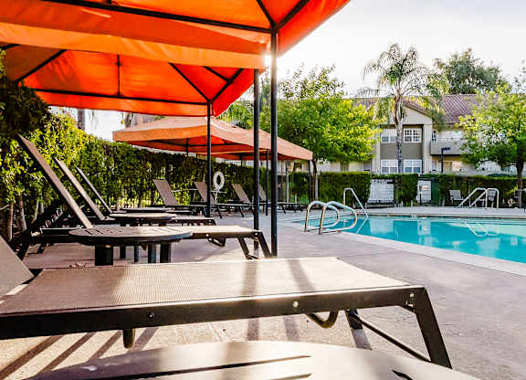 A poolside area with sun loungers and an orange umbrella. at Legends at Rancho Belago, Moreno Valley