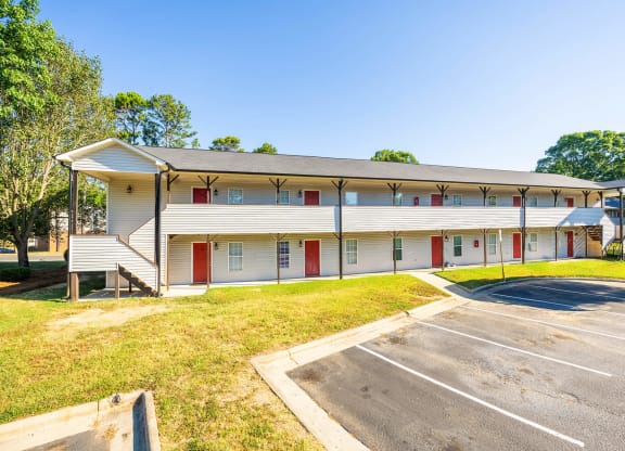 a white building with red doors and a parking lot at Ashford Place Apartments, Kannapolis, 28081