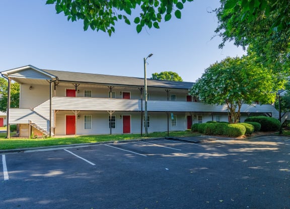 an empty parking lot in front of a white building with red doors at Ashford Place Apartments, Kannapolis, NC