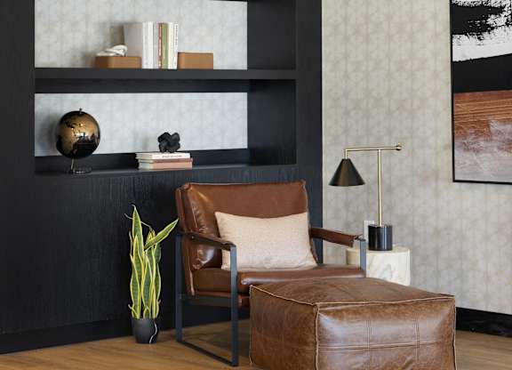 A brown leather chair sits in front of a shelf with a plant and a globe on it.