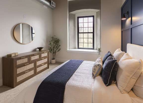A bedroom with a large bed and a mirror on the wall at The Dean at Creekview Apartments, Newark, Delaware
