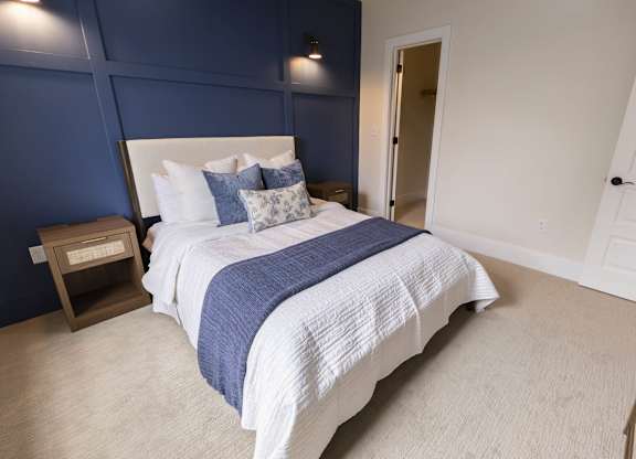 A bed with a white headboard and a blue and white comforter at The Dean at Creekview Apartments, Delaware