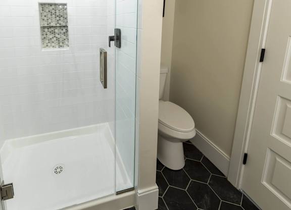 A white toilet sits next to a walk-in shower in a bathroom. at The Dean at Creekview Apartments, Newark, DE, 19711