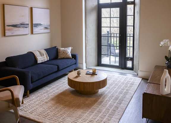A living room with a blue couch and a large window at The Dean at Creekview Apartments, Newark