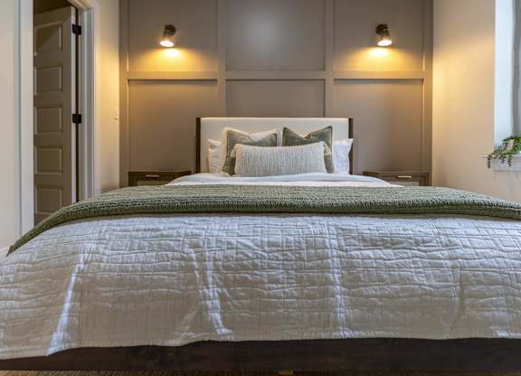A bed with a white comforter and a green throw at The Dean at Creekview Apartments, Newark, DE, 19711