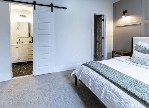 A bedroom with a bed, nightstand, and a sliding door leading to a bathroom at The Dean at Creekview Apartments, Newark