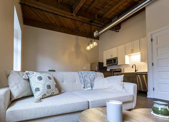 A white couch with a grey pillow is in the middle of a room at The Dean at Creekview Apartments, Newark, Delaware