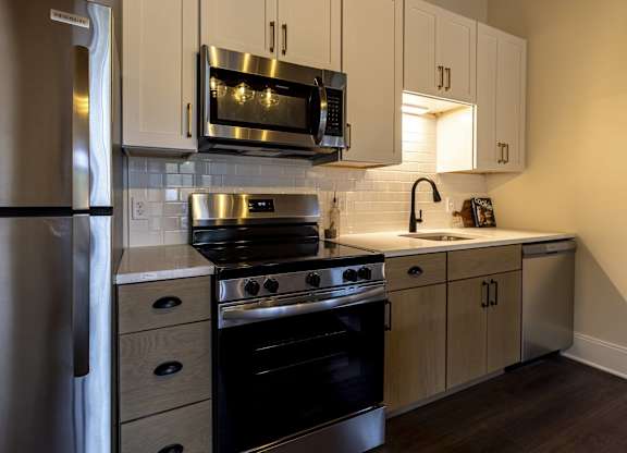 A modern kitchen with a stainless steel refrigerator, black stove, and wooden cabinets at The Dean at Creekview Apartments, Delaware