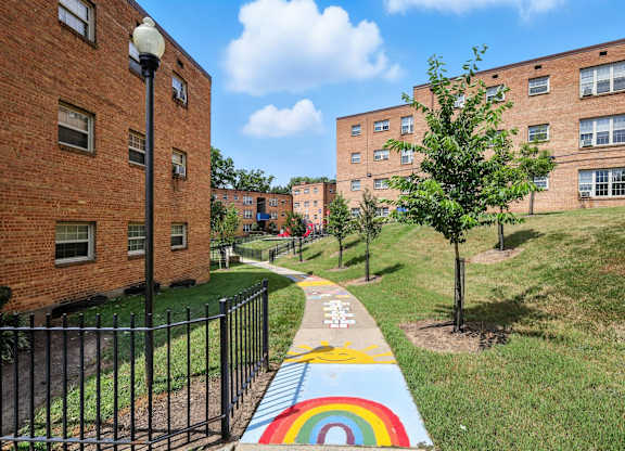 A rainbow painted on a sidewalk in front of a black fence at Huntwood Courts Apartments, Washington DC
