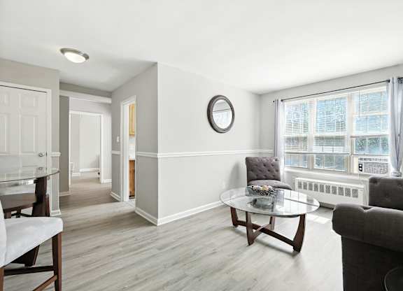 A living room with a grey couch, a coffee table, and a window with a view of a building outside at Huntwood Courts Apartments, Washington DC