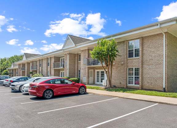 A red car is parked in a parking lot in front of a brick building at The Overlook at Quantico Apartments, Triangle, VA, 22172