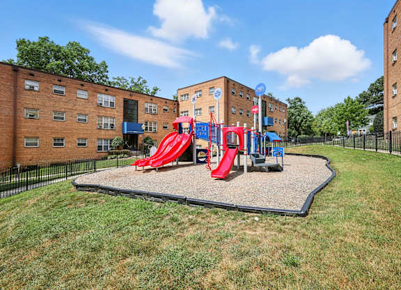 A playground with a red slide and a blue slide in the middle of a grassy area at Huntwood Courts Apartments, Washington DC