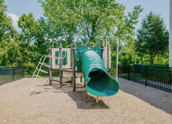 a large green slide in a park with trees in the background