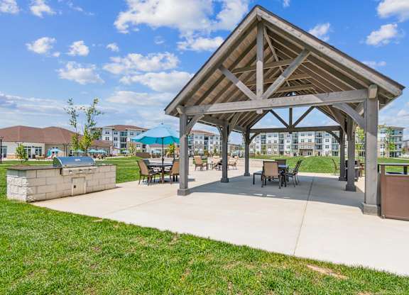 A pavilion with a roof and chairs is surrounded by a grassy area.