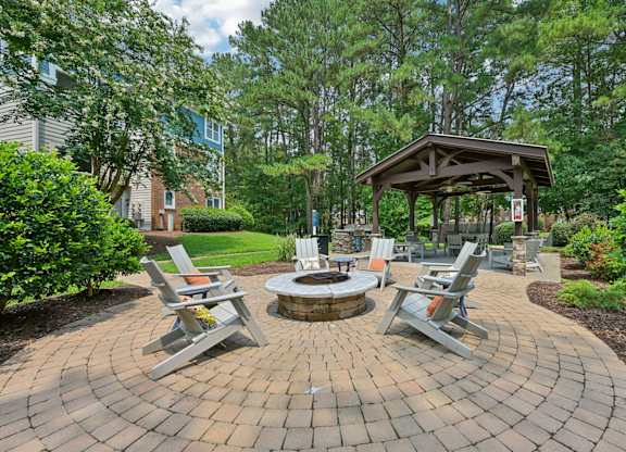 A fire pit is surrounded by four chairs in a backyard.