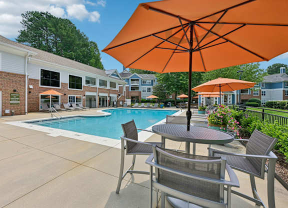 A large orange umbrella is in the foreground of a pool area.