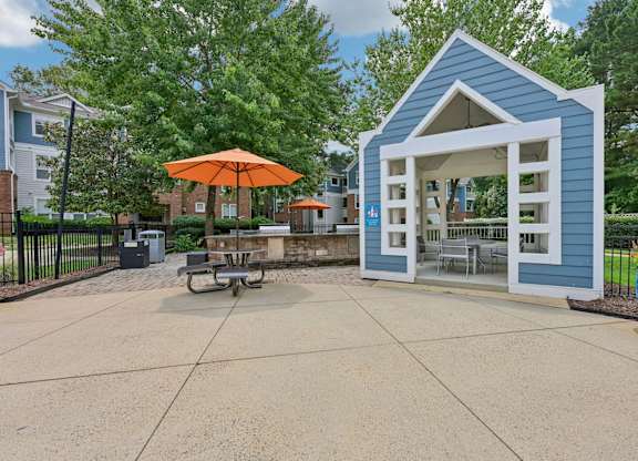 A small blue building with an orange umbrella sits in the middle of a paved area.