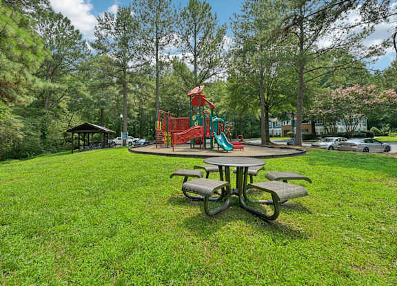 A playground with a red slide and a green slide is surrounded by trees.