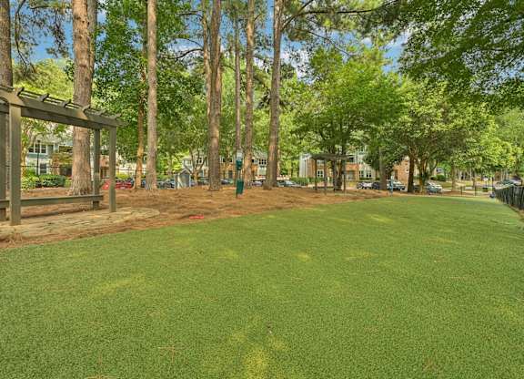 A green lawn with trees and a wooden structure in the background.