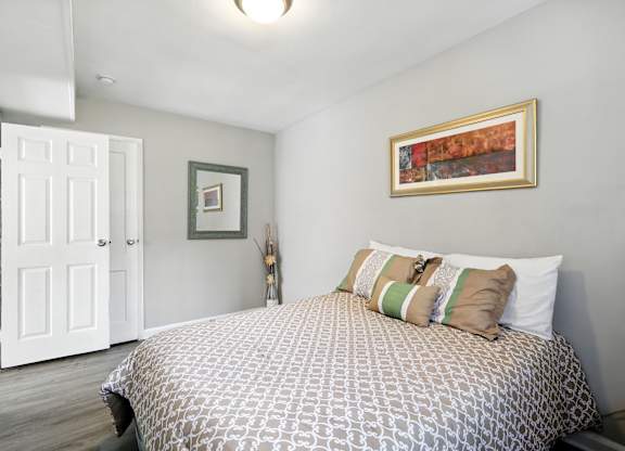 A bedroom with a bed, pillows, and a painting on the wall at Huntwood Courts Apartments, Washington DC