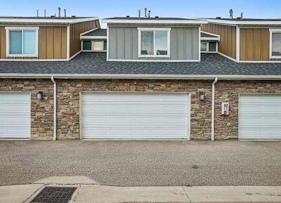 A house with a stone wall and three garage doors.