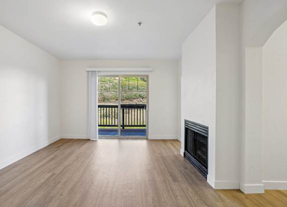A large empty room with a fireplace and a view of a balcony.