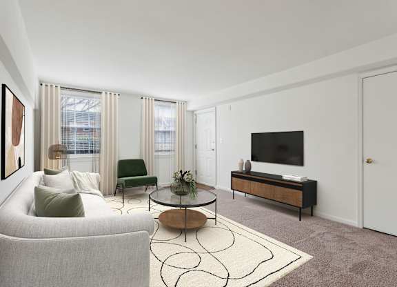 A living room with a grey couch, a green chair, a coffee table, and a television at The Fields of Bethesda, Chevy Chase, MD