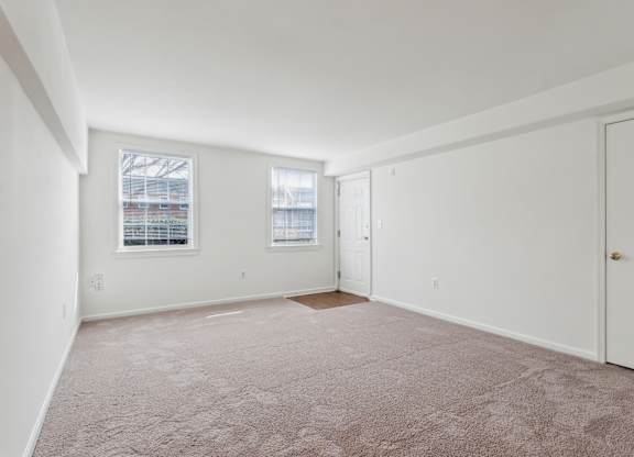 A room with a carpeted floor and two windows.