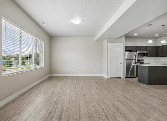 A spacious room with wooden flooring and a kitchen area in the background.