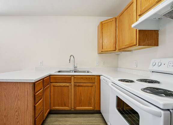 A kitchen with a white stove top oven and wooden cabinets.