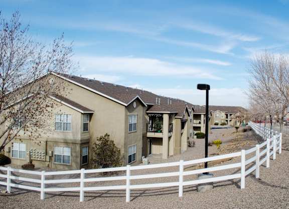 A white fence surrounds a building with a brown roof at Arrowhead Ridge Apartments, New Mexico 87124