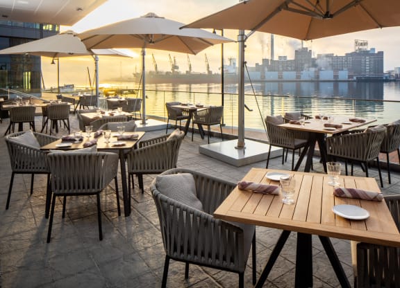 a restaurant with tables and chairs and umbrellas overlooking the water at Allied Harbor Point, Baltimore, MD, 21231