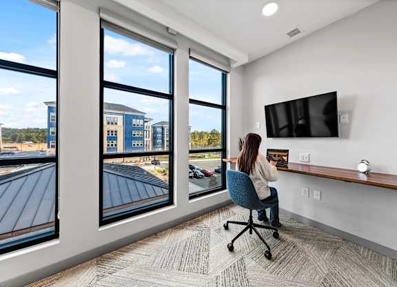 A woman is sitting at a desk in a private office with a large window at Preston Ridge Apartments Cary, NC.