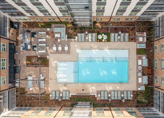 A large swimming pool is surrounded by a patio with lounge chairs and umbrellas at Hawkins Press Apartments, Charlotte, 28203
