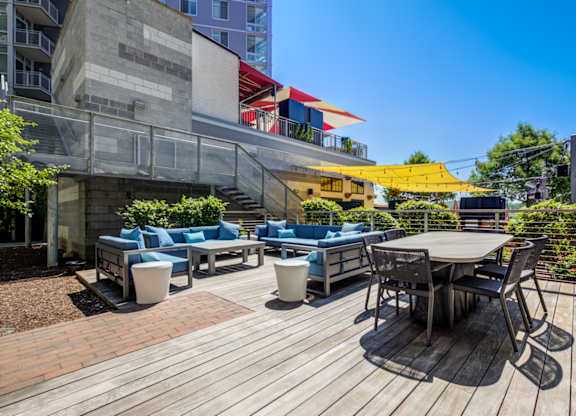 A wooden deck with a table and chairs in the foreground and a building in the background.