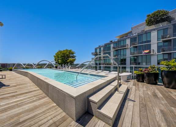 A wooden deck with a pool and a building in the background.