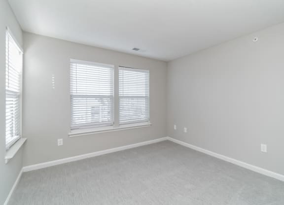 an empty bedroom with two windows and white carpeting at The Fields at Lorton Station, Lorton, VA