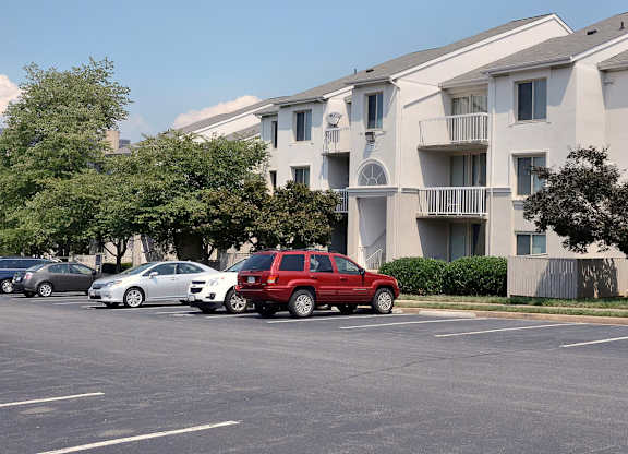 A red car is parked in a parking lot in front of apartment buildings.